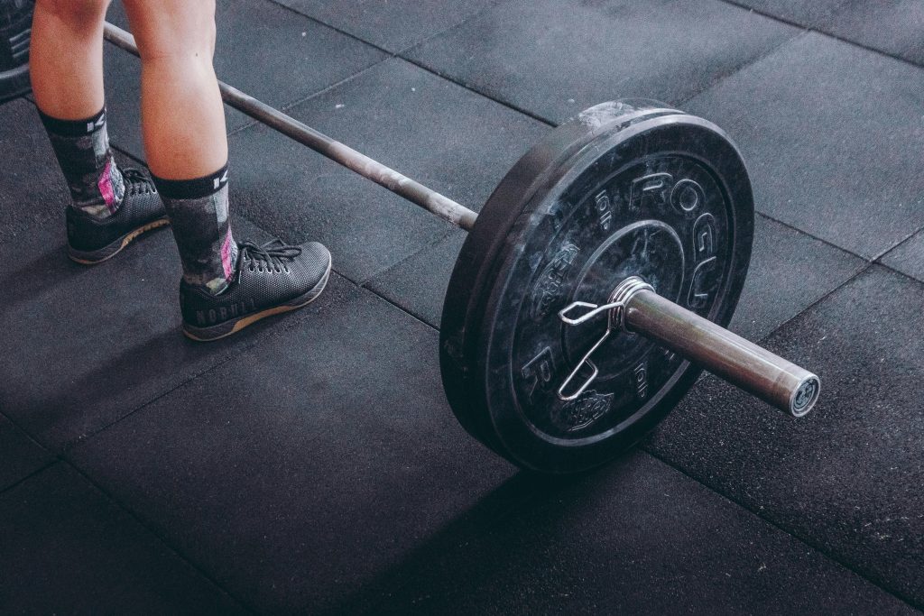 Close-up of an athlete's legs beside a barbell, ready for weightlifting in a gym.