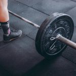Close-up of an athlete's legs beside a barbell, ready for weightlifting in a gym.