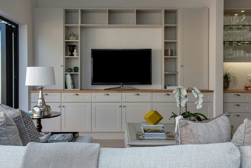 Narrow tall bookshelf in a compact apartment with organized baskets, books, and decorative items.